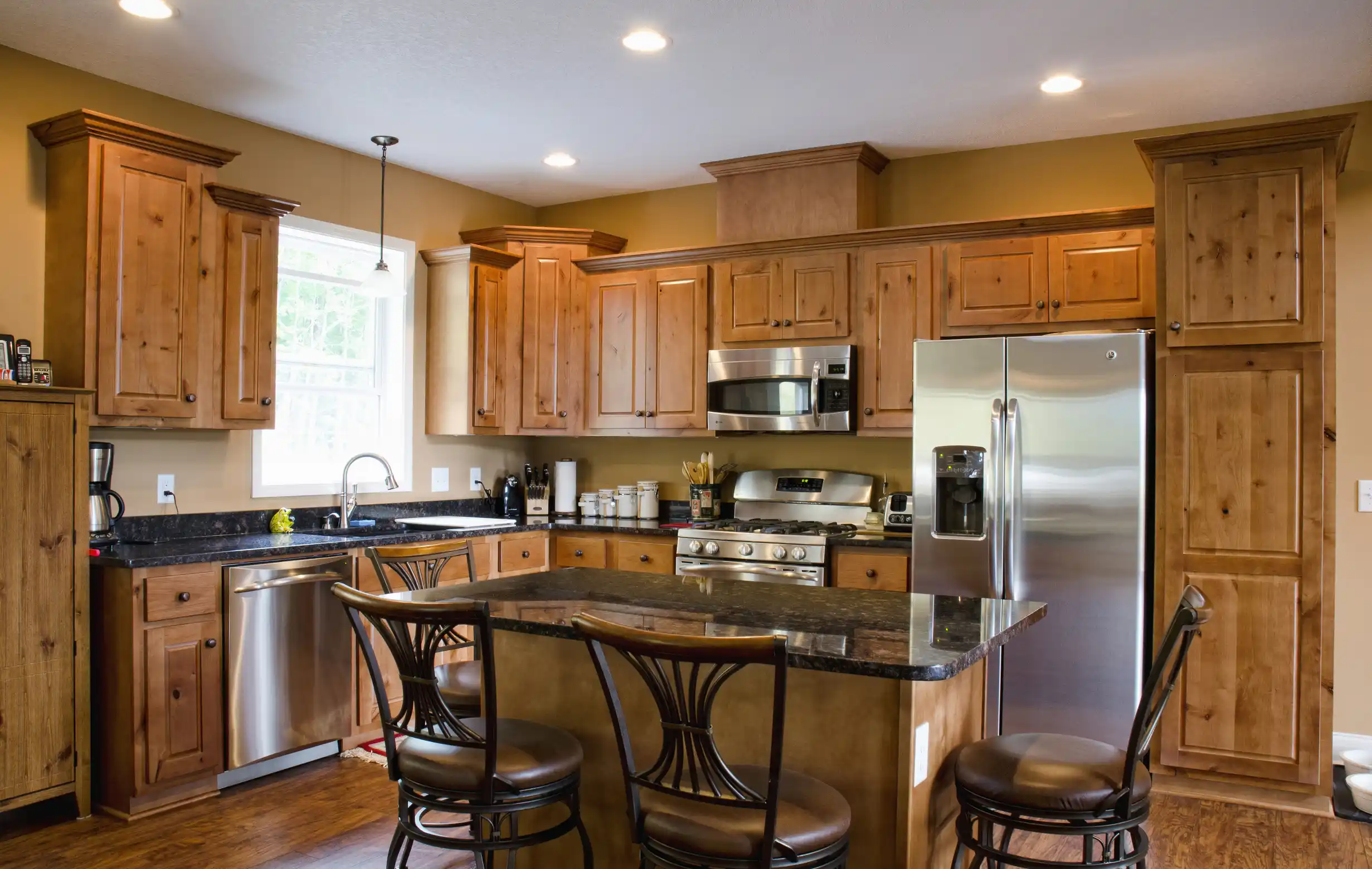 Spacious kitchen with wood cabinets, a large island with a stone countertop, stainless steel appliances, and four chairs.