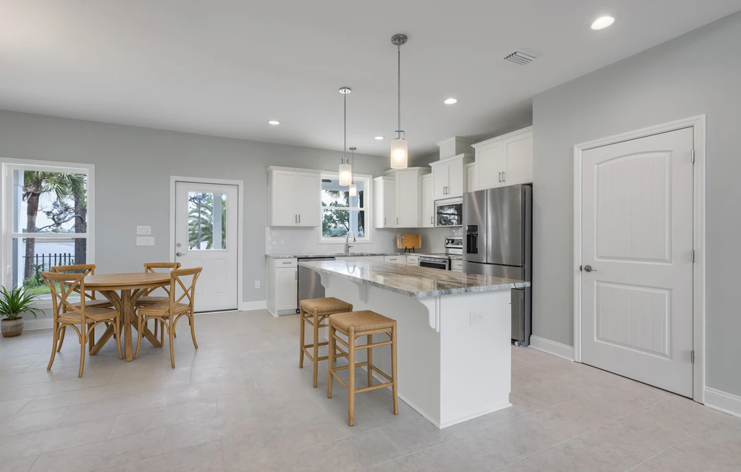 Kitchen with light-colored cabinetry, granite countertops, stainless steel refrigerator, and a dining table with chairs; two stools sit at the counter and a potted plant adds