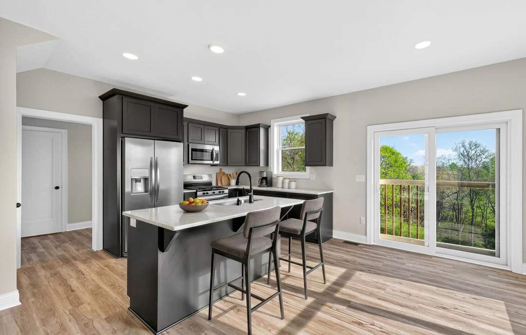 Kitchen with a bar area featuring stools, light-colored cabinetry, granite countertops, a bowl of fruit, stainless steel appliances including a microwave and refrigerator, laminate