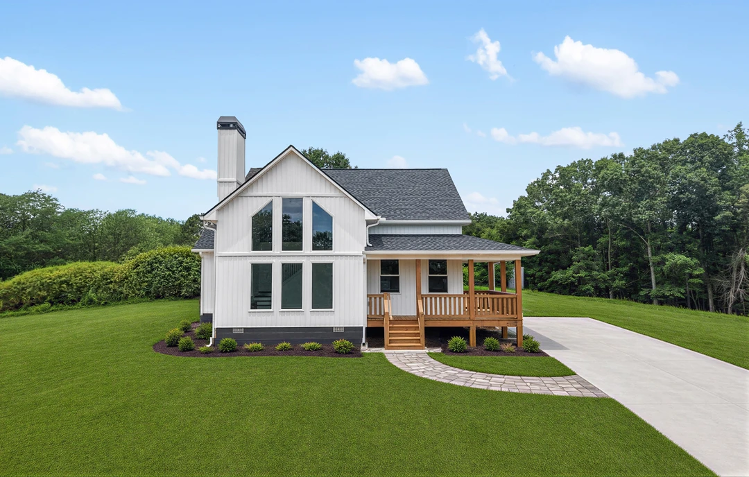 White farmhouse-style home with a covered porch, wooden deck, and large windows, set on a grassy lawn with landscaping and mature trees in the background.