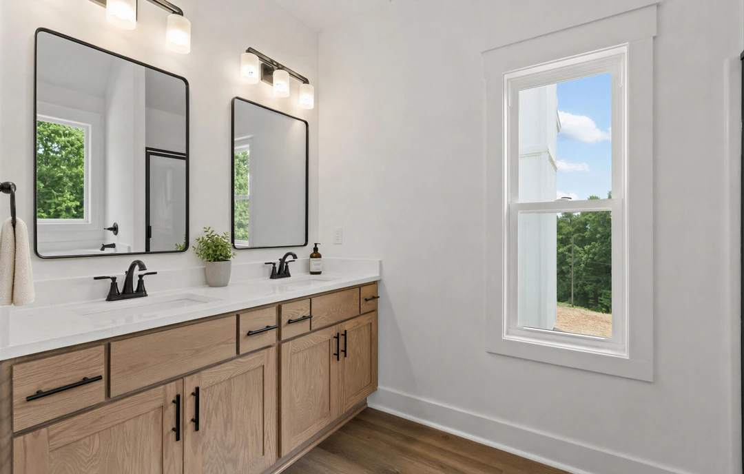 Bathroom with a double sink vanity featuring black-framed mirrors, white cabinetry, granite countertops, a window with a white frame, a metal hook holding a white towel, and a