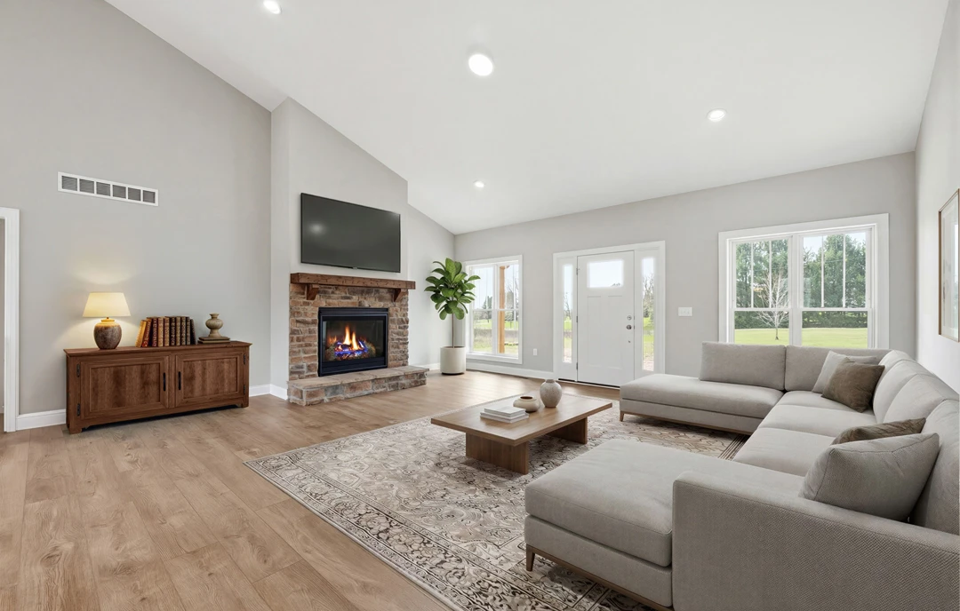 Living room with hardwood flooring, a gray couch with pillows, a fireplace with fire, a wall-mounted TV, a wooden cabinet with books, and a potted plant.