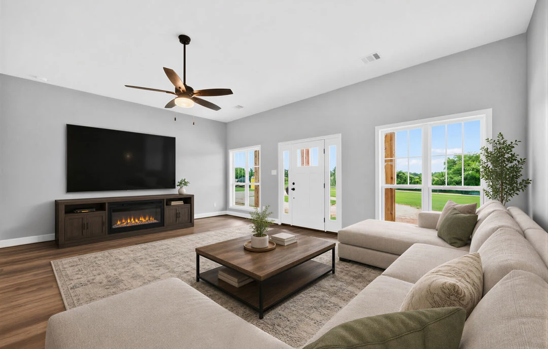 Living room with a television mounted above a fireplace, a coffee table with a potted plant, gray couches, and a ceiling fan with a light fixture.