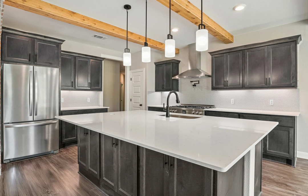 Kitchen with a large central island featuring white granite countertops, white cabinetry, stainless steel appliances including a refrigerator and oven, and multiple pendant lights
