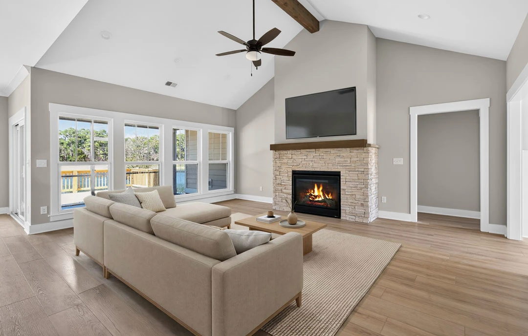 Living room with a wood-burning fireplace, gray couch, wood flooring, ceiling fan with light, and a black television mounted above the mantel.