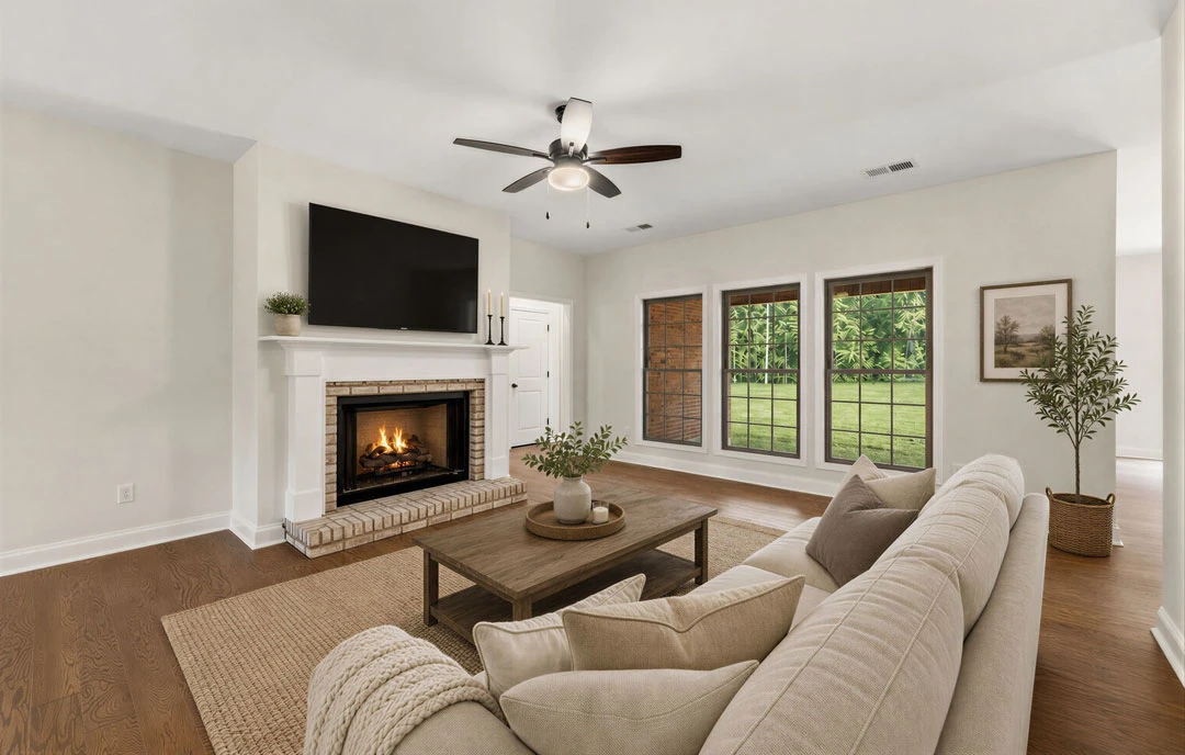 Living room with a stone fireplace, gray couch, ceiling fan with light, wood flooring, coffee table, and a potted tree near the wall.