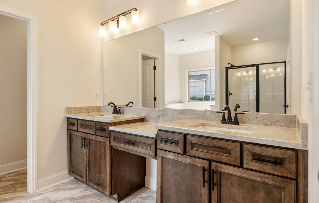 Bathroom with double sink vanity, granite countertop, large mirror above, glass shower door, white cabinetry with black handles, and tile flooring.