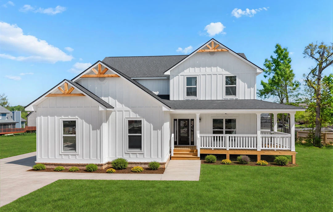 White farmhouse-style exterior with black roof, white porch railing, and a green lawn bordered by mature trees.