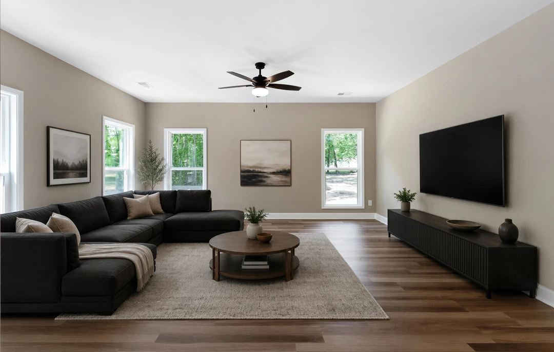 Living room with a large gray couch, a wall-mounted television with a black screen, a coffee table holding a bowl, laminate wood flooring, a ceiling fan with a light, and landscape