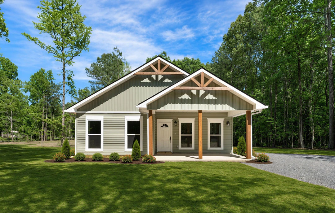 Two-story farmhouse with white siding, a covered porch, white-framed windows, and a gravel driveway bordered by grass and mature trees.
