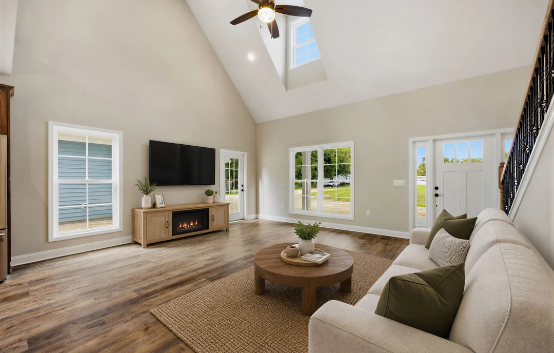 Living room with a gray couch and pillows, round wooden coffee table with a plant, wall-mounted television above a fireplace, wood or laminate flooring, and a ceiling fan with a