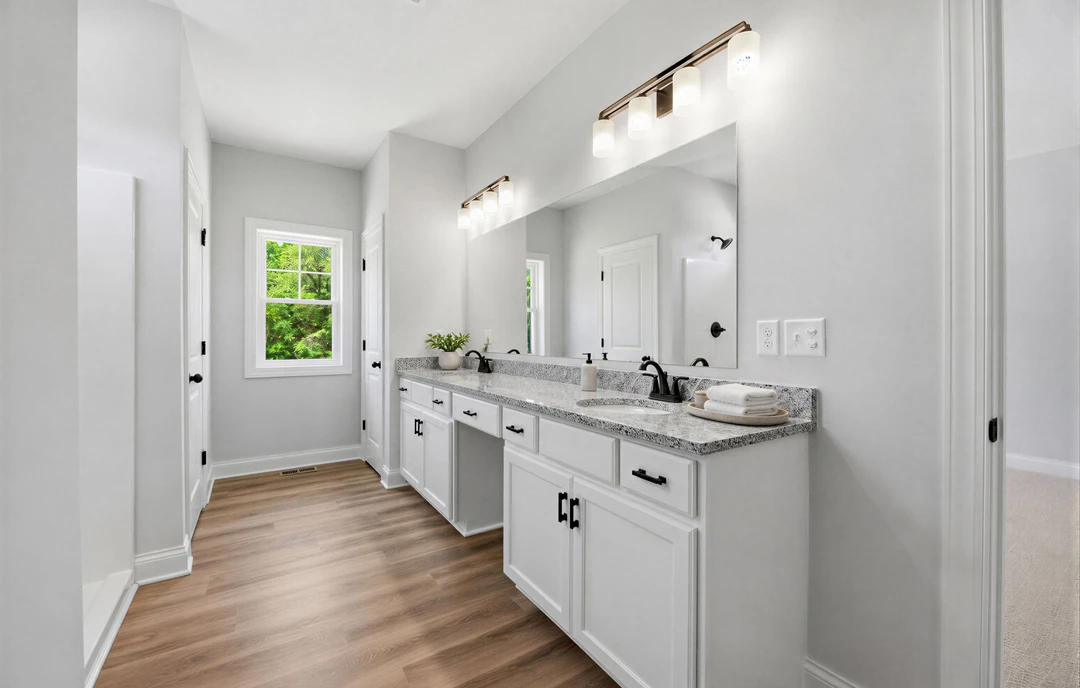 Bathroom with white cabinets, a mirror above the sink, wood flooring, a window showing trees outside, a stack of white towels on a plate, and a four-light fixture overhead.