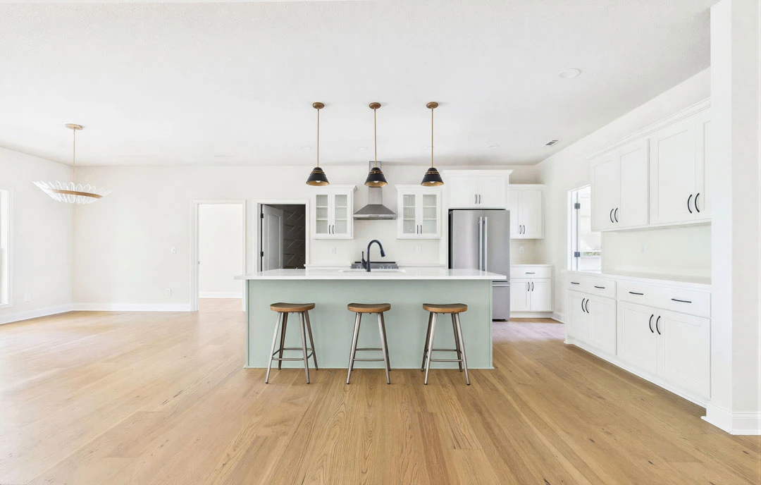 Kitchen with a central island featuring a white granite countertop, several wooden stools, light wood cabinetry, and laminate flooring.