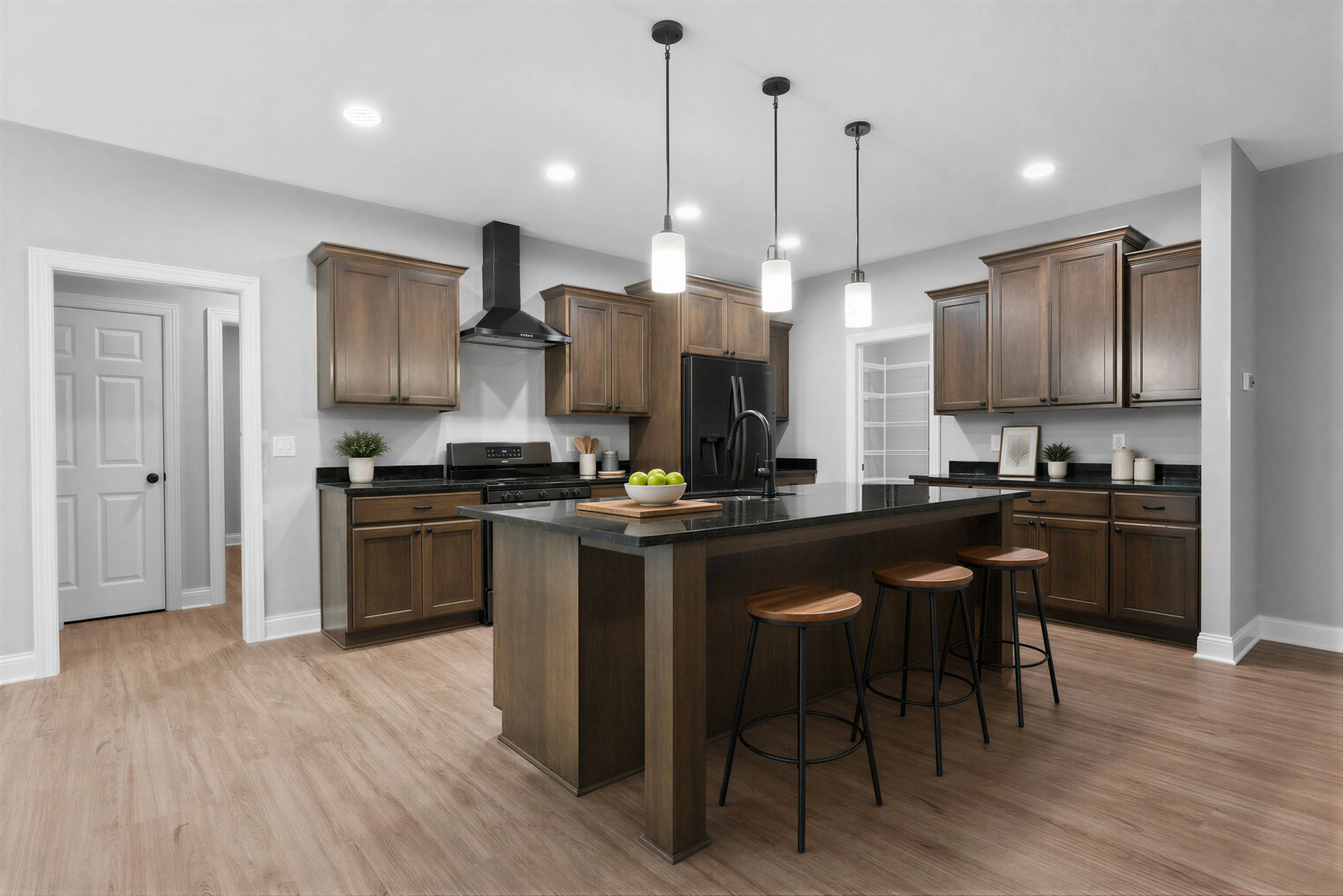 Modern kitchen with a central island and wooden stools, white cabinetry, black refrigerator and faucet, granite countertops, light wood flooring, and a bowl of green apples on the