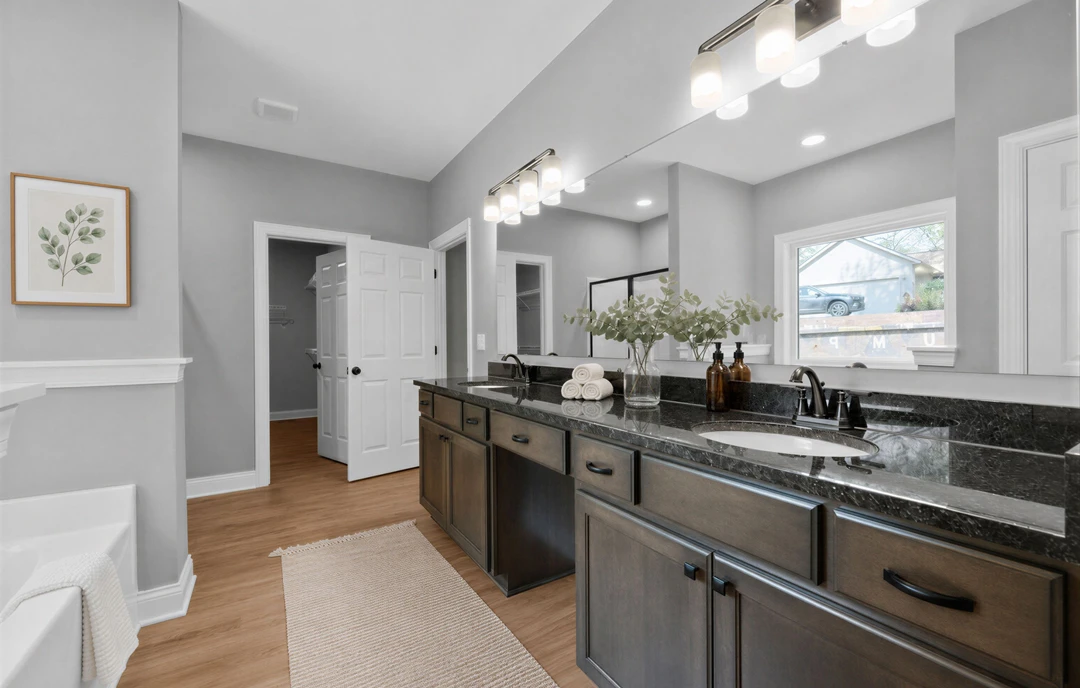 Bathroom with a large mirror above a wide sink and countertop, light cabinetry below, a framed plant picture on the wall, bottles and a vase on the counter, a white towel on the