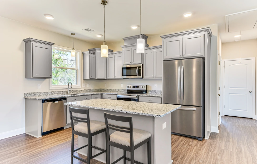Modern kitchen with a granite countertop bar, stainless steel appliances including a refrigerator, dishwasher, and microwave with the door open, light cabinetry, and chairs along