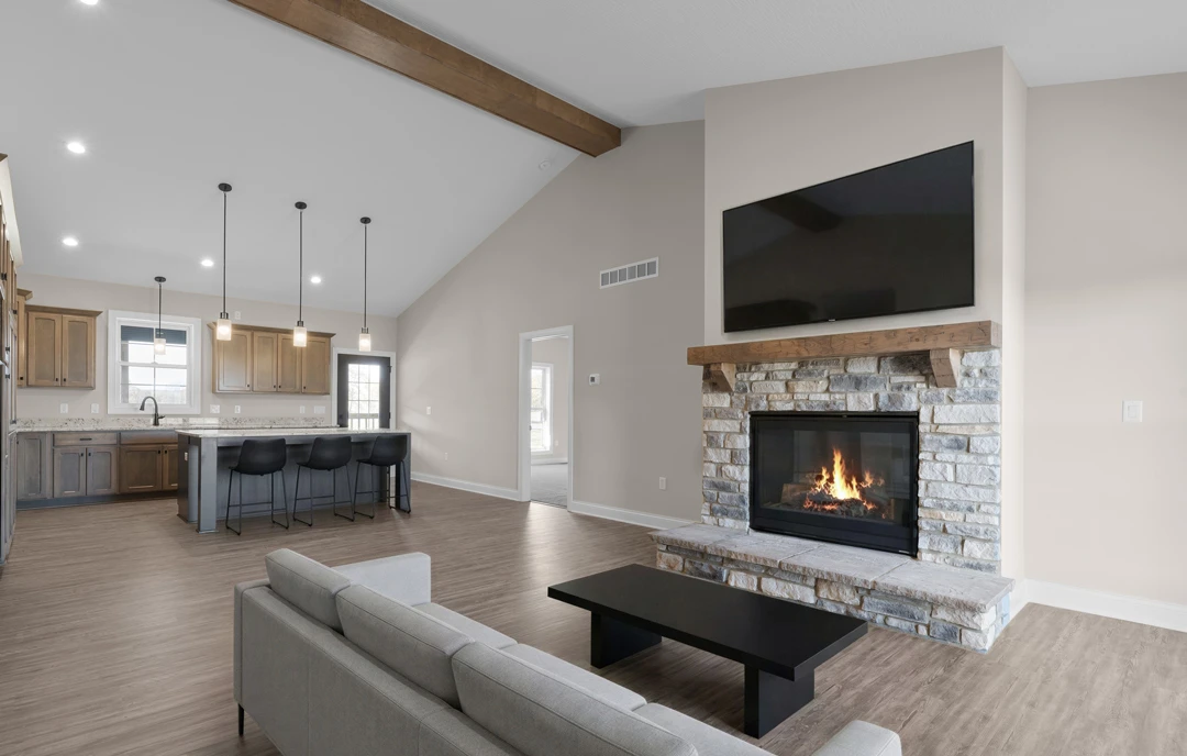 Living room with a lit fireplace, black coffee table, couch, and black chairs, open to a kitchen with stone countertops.