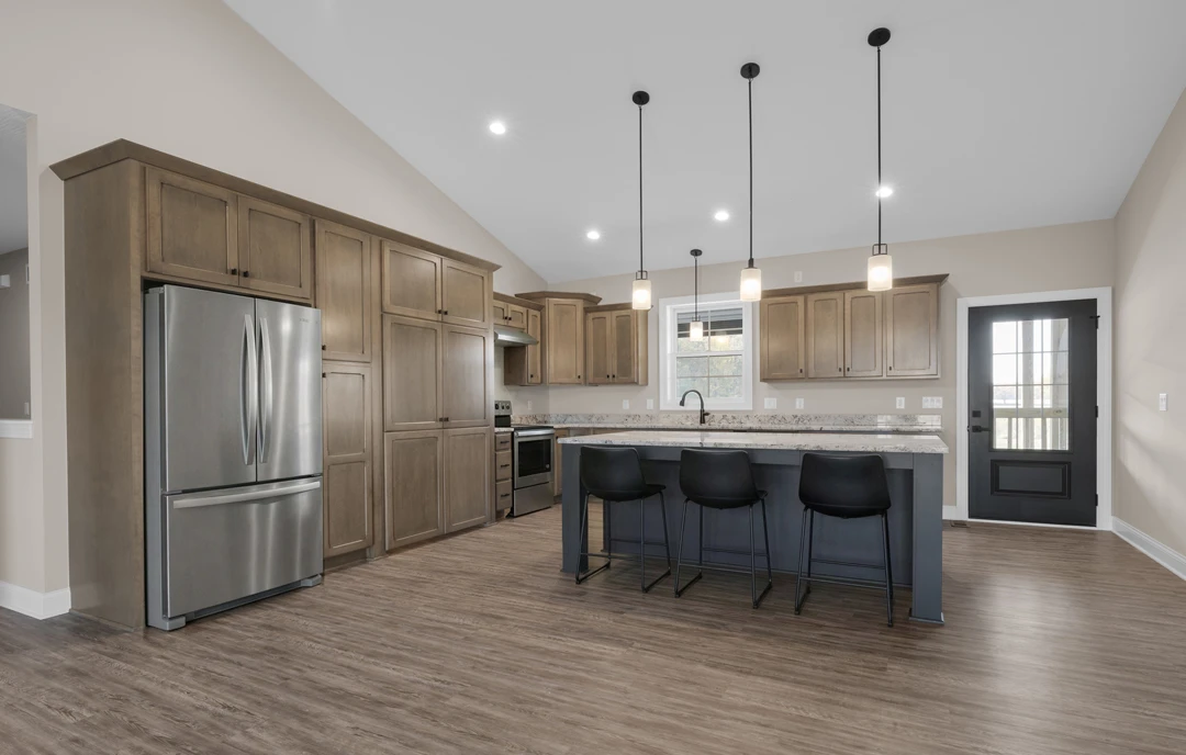 Kitchen with light plywood cabinetry, granite countertops, a stainless steel refrigerator, a bar area with black stools, and laminate flooring.