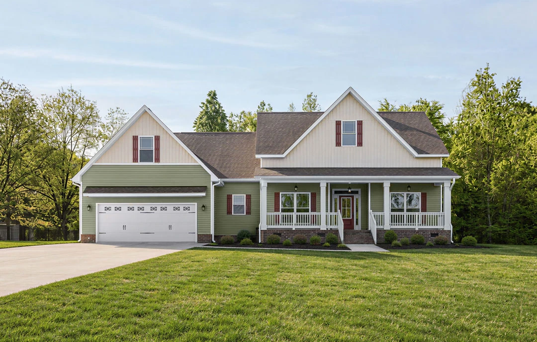 Green house with white trim and red shutters, featuring a white front door, attached garage, and a well-kept lawn bordered by trees.