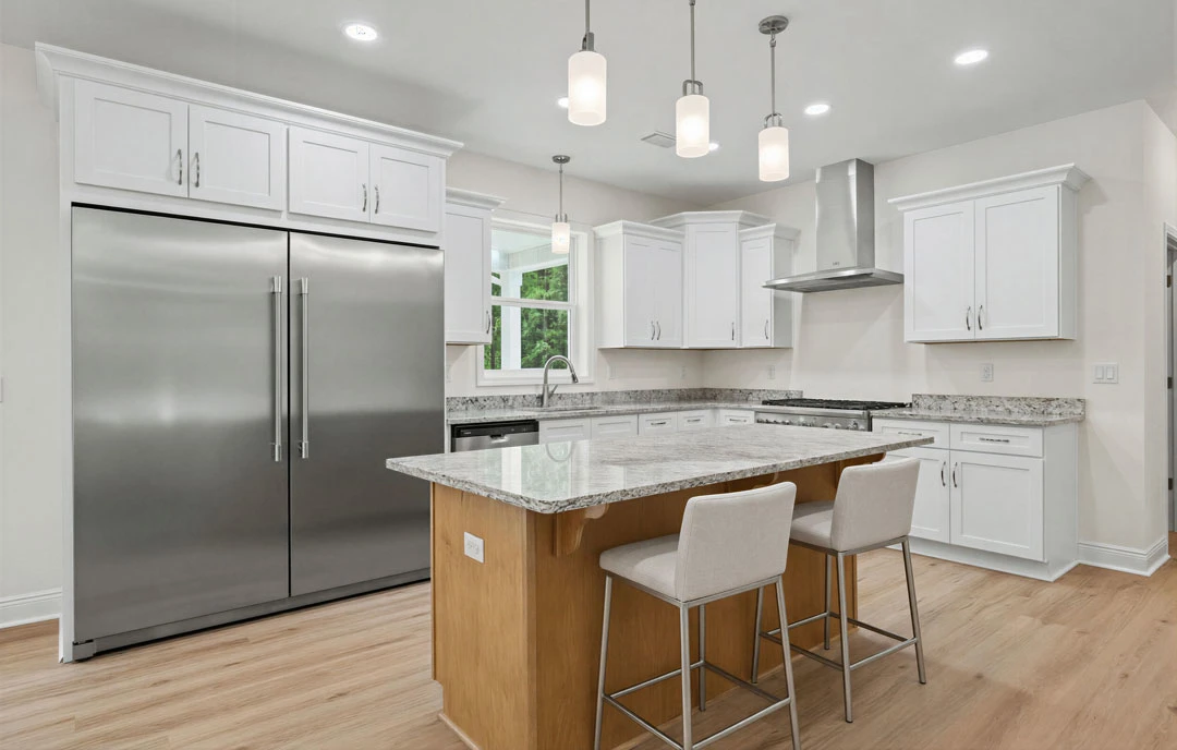 Kitchen with a large granite island featuring bar chairs, stainless steel double-door refrigerator, white cabinetry, and pendant lights hanging from the ceiling.