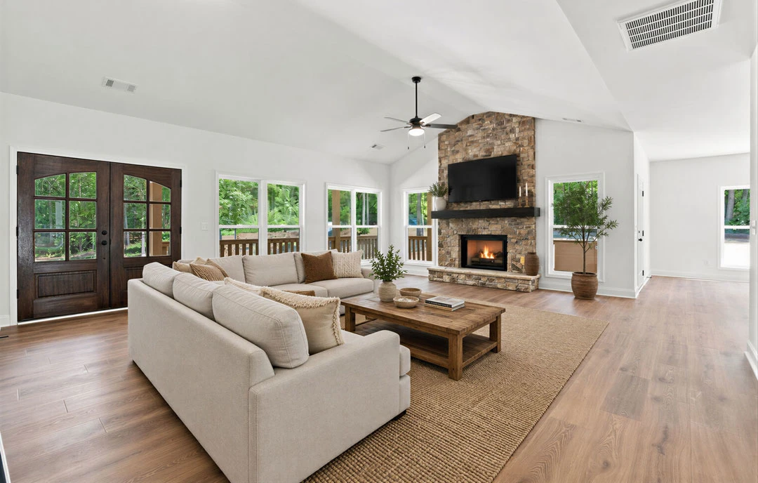Living room with hardwood flooring, a gray couch facing a fireplace with a fire burning, a coffee table holding bowls and books, glass-paneled double doors, and a small potted tree
