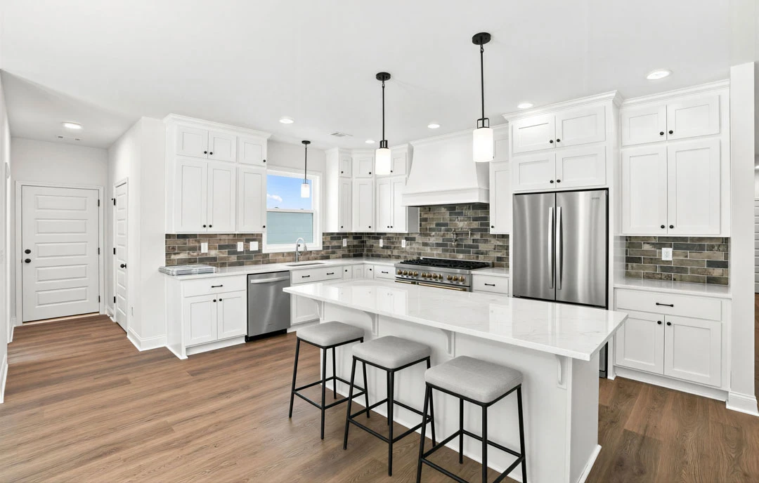 Kitchen with white cabinets and a large white island, granite countertops, stainless steel refrigerator, cushioned stools at the island, and light-colored flooring.