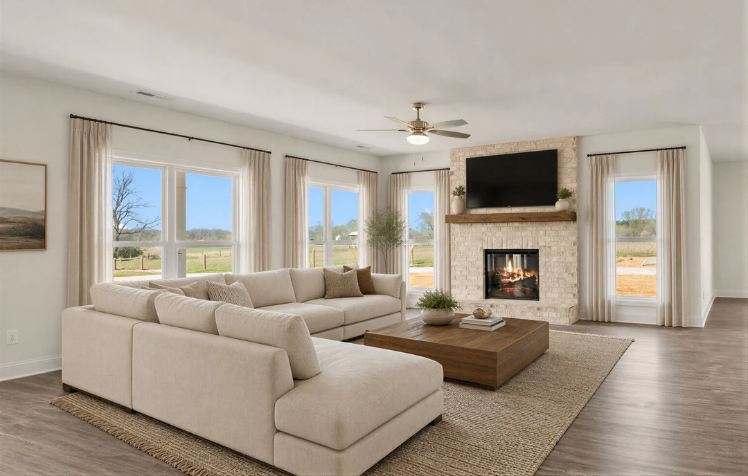 Living room with a large sectional couch facing a brick fireplace, a coffee table in front, and a window with curtains showing trees outside.