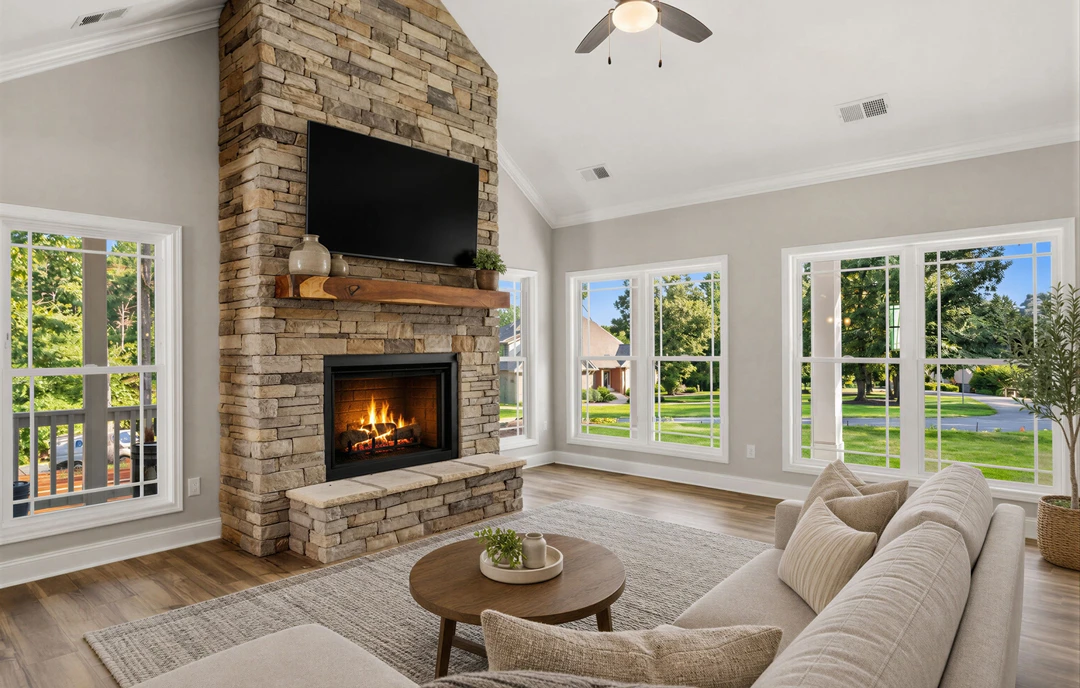Living room with a brick fireplace and mounted television, round wooden coffee table with a plant, ceiling fan with light, and upholstered couches on hardwood flooring.