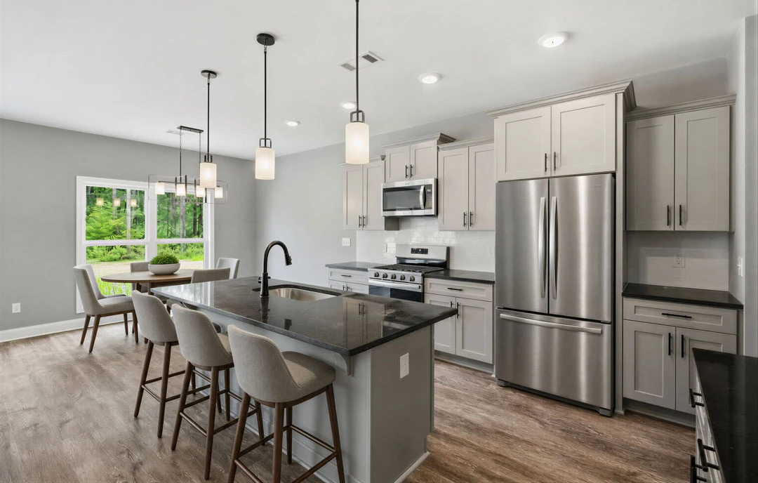 Spacious kitchen featuring a large central island with granite countertops, white cabinetry, stainless steel appliances, a sizable dining table with chairs, and wood flooring.