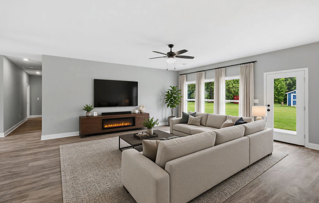 Living room with a large sectional sofa, fireplace, ceiling fan with light, white curtains, laminate or wood flooring, and a potted plant.
