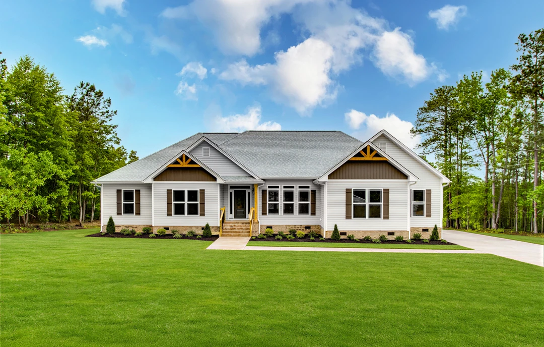 Two-story house with a covered front porch, white trim, and stairs leading to a landscaped lawn with mature trees and a walkway, set against a blue sky with scattered clouds.
