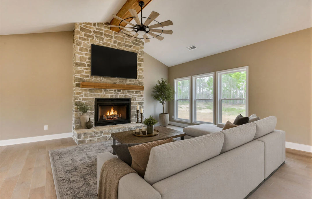 Living room with a brick fireplace beneath a wall-mounted TV, a gray couch with pillows, wood flooring, a potted tree, and a ceiling fan with wood blades.