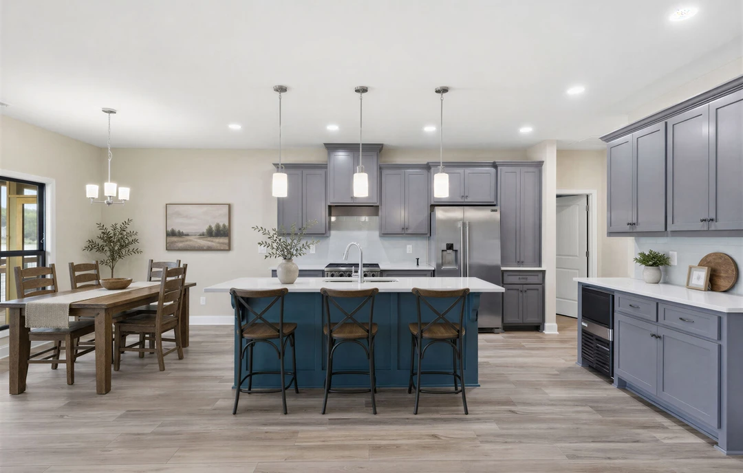 Kitchen with a large central island featuring white granite countertops, white cabinetry, a wooden-seated chair, and a dining table with a bowl, with a landscape painting hanging