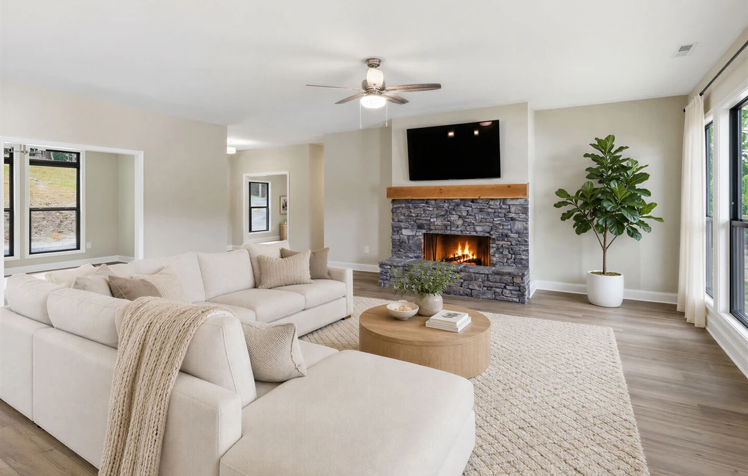 Living room with a fireplace, wood or laminate flooring, a gray couch with pillows and a blanket, a potted plant in a white pot, a coffee table with bowls, and a ceiling fan with a
