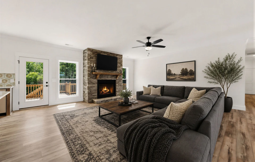 Living room with a gray couch decorated with pillows and a blanket, wood or laminate flooring, a fireplace with a fire burning, a coffee table holding a vase, a potted plant beside