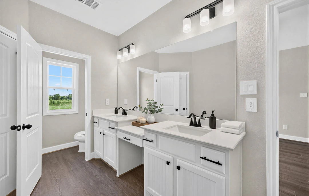 Bathroom with white cabinets and white countertops, a window overlooking a field and trees, a plant in a vase, a stack of white towels, and tile flooring.