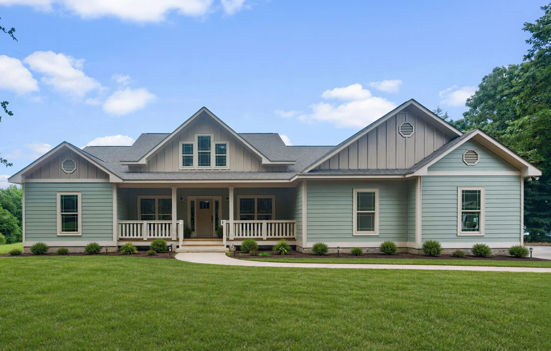 Two-story farmhouse with light-colored siding, a covered front porch with white railings, a lawn with a walkway, and bushes near the entrance; Robert Frost Farm visible in the