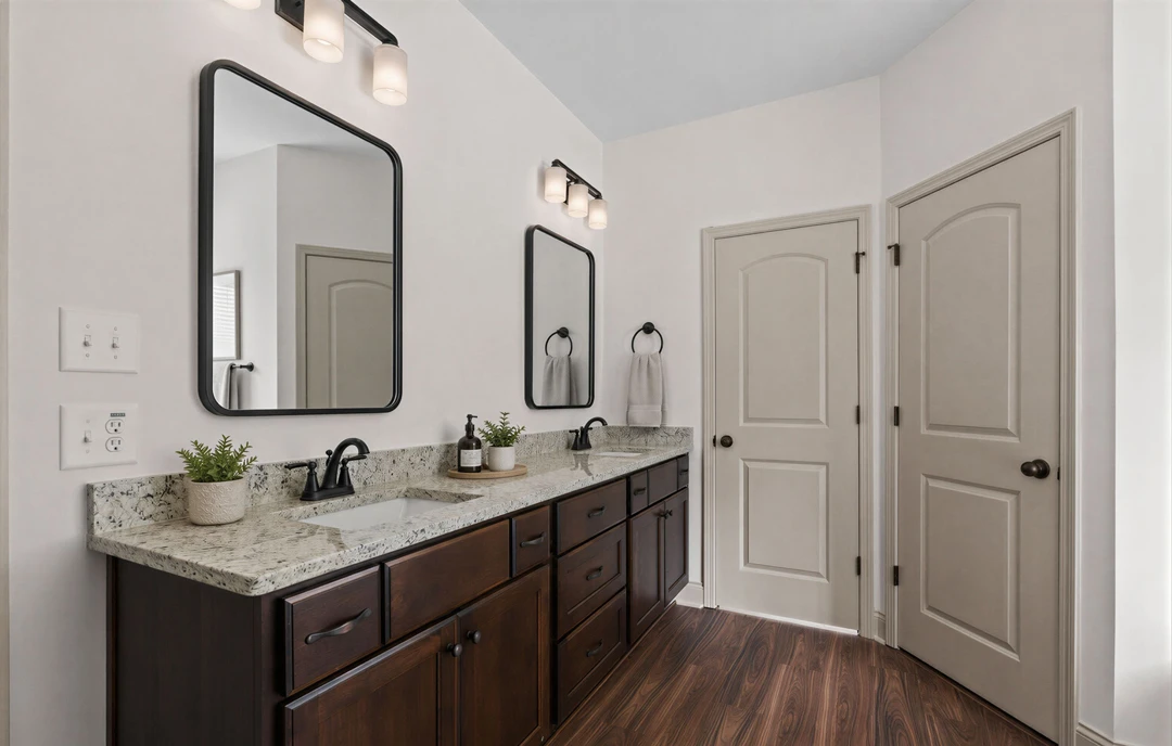 Bathroom with double sinks set in a granite countertop, two rectangular mirrors above, white cabinetry below, and a potted plant on the counter; white tile flooring and a white