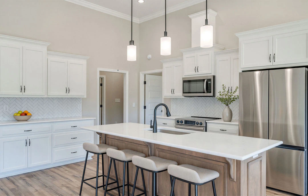 Kitchen with a central island featuring granite countertops and stools, stainless steel refrigerator, white cabinetry, tile flooring, and a vase with green leaves on the island.
