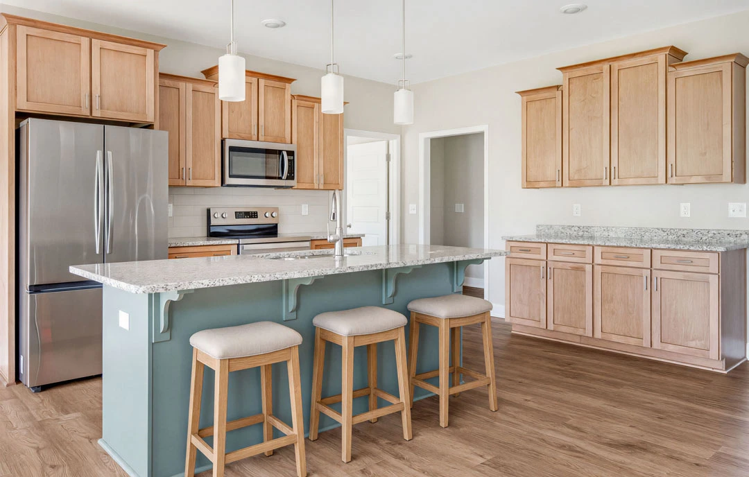 Kitchen with light cabinetry, granite countertops, stainless steel appliances including a microwave and refrigerator, and a bar area with two cushioned stools.