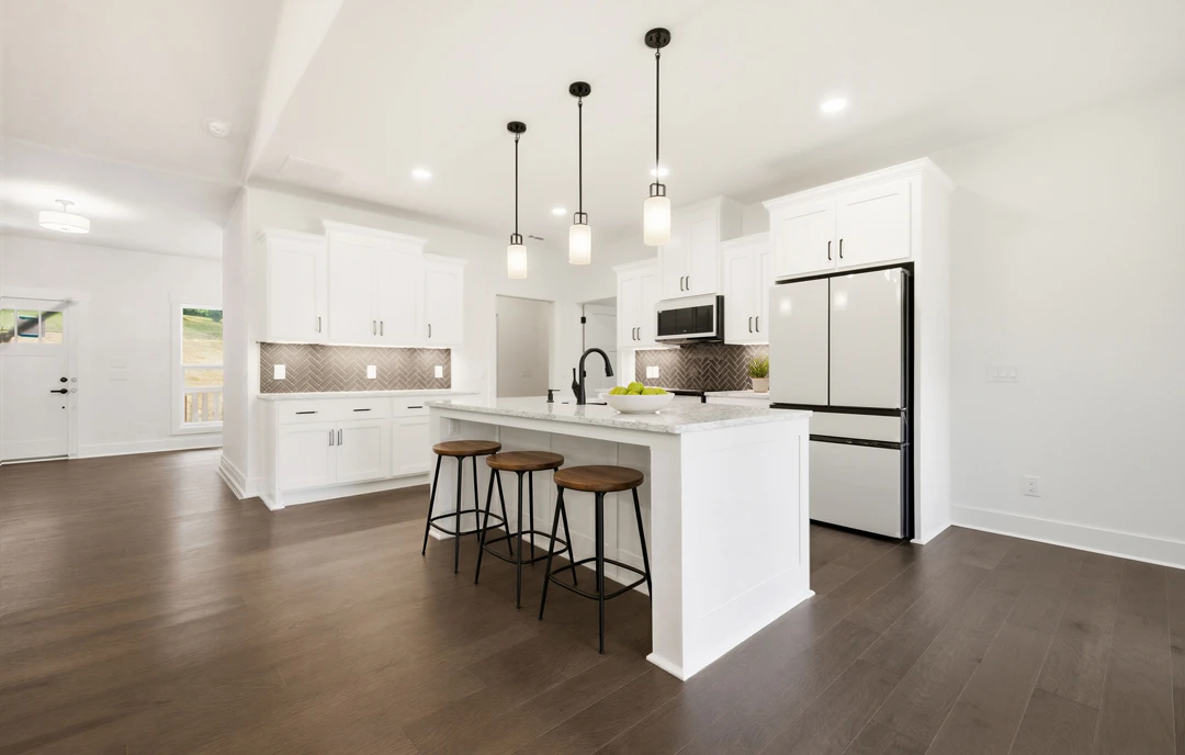 White kitchen with granite countertops, white cabinetry, a bar area with black stools, a white refrigerator, microwave, and a bowl of fruit on the counter, with laminate wood