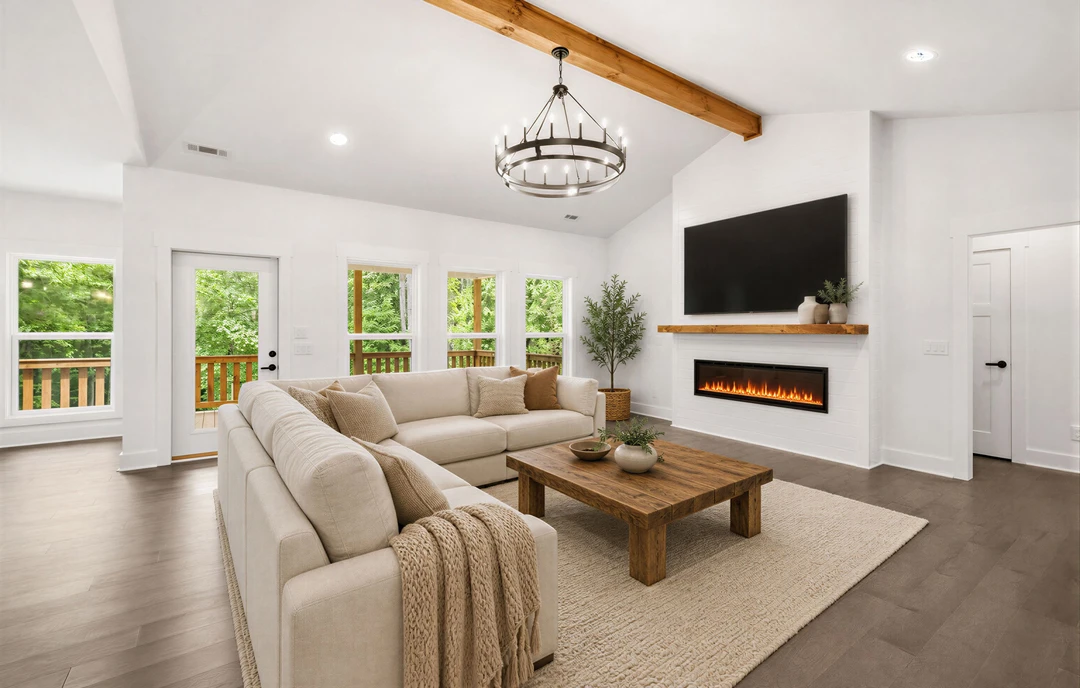 Living room with hardwood flooring, a fireplace, a gray couch draped with a blanket, a wooden coffee table holding two potted plants, a chandelier overhead, and a potted tree near
