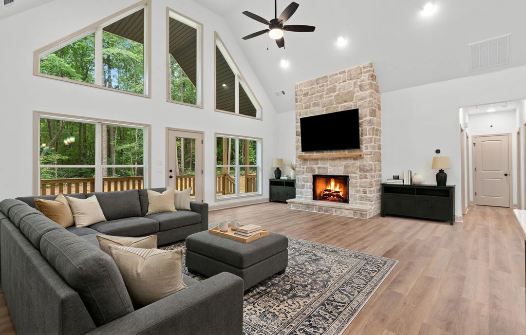 Living room with a brick fireplace, gray couch with pillows, wood or laminate flooring, black cabinet with a shelf, ceiling fan with light, and a white door with black hardware.