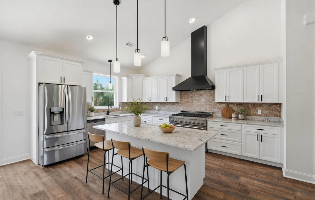 Kitchen with a large island featuring granite countertops, white cabinetry, stainless steel refrigerator and stove, bar stools, and a plant in a vase on the counter.