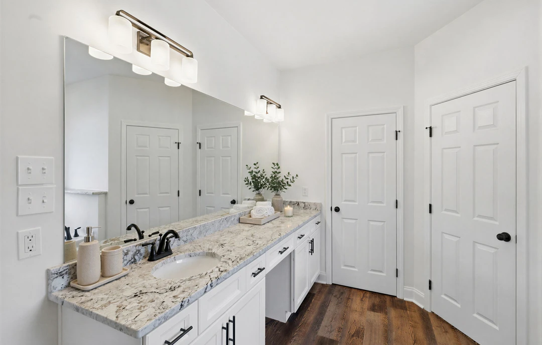 Bathroom with white cabinets, granite countertop, white oval sink, black hardware, and decorative vases with plants and towels.