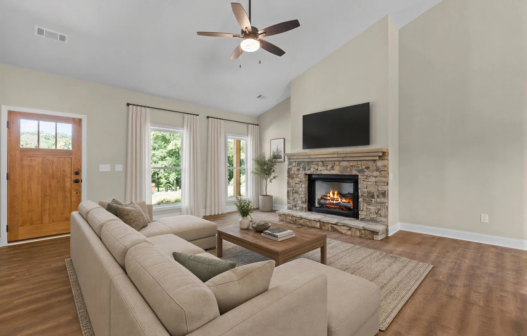 Living room with a lit fireplace, gray couch with pillows, wood flooring, and a ceiling fan with light fixture.