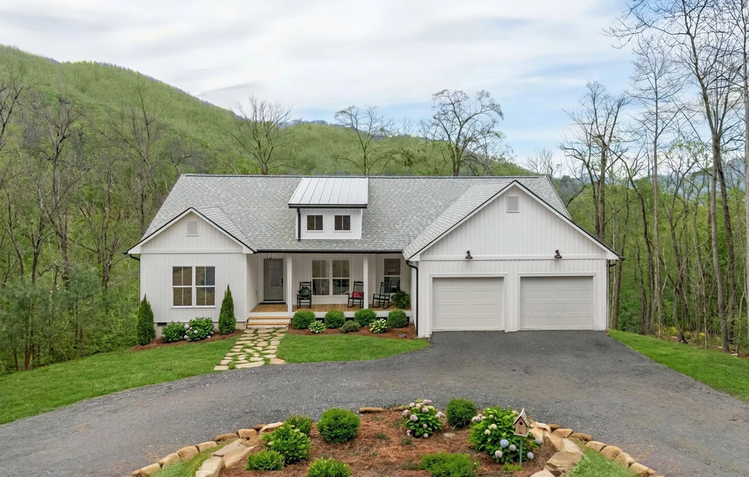 Two-story house with light-colored siding, attached garage, covered front porch, and a stone walkway leading through a landscaped lawn with bushes and trees.