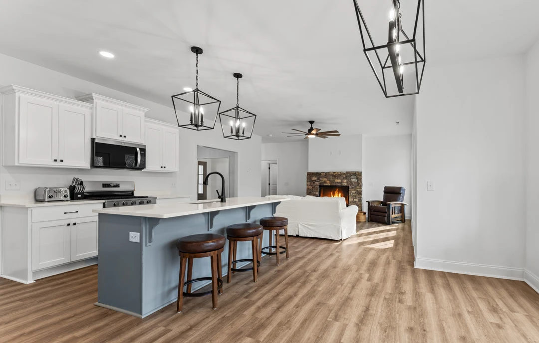 Open-concept kitchen and living room featuring white cabinetry, granite countertops, stainless steel appliances, laminate flooring, and a fireplace with a stone surround.
