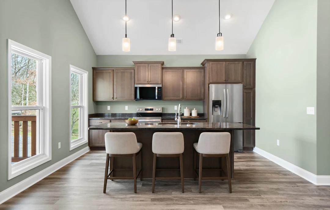 Kitchen with white cabinetry, granite countertops, a central island with chairs, stainless steel appliances including a microwave and refrigerator, laminate flooring, and a window