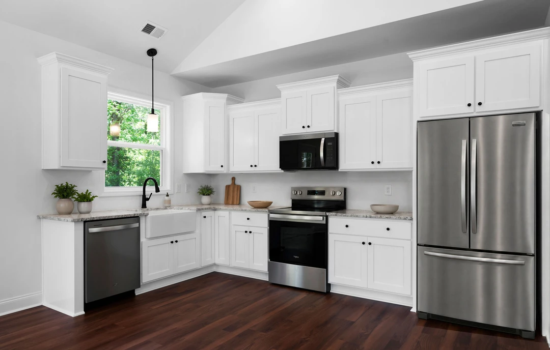 Kitchen with white cabinets, stainless steel appliances including refrigerator, stove, microwave, and black dishwasher, granite countertops, and wood flooring.